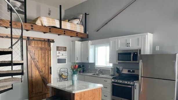 A kitchen with a wooden island, stainless steel appliances, and a staircase with a wooden finish. - Doney Creek Studio (Lakehead-Lakeshore)