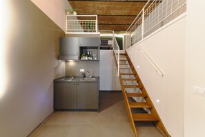 Una cucina compatta con piano cottura integrato, lavello e pensili, una scala in legno e un piccolo balcone con piante.