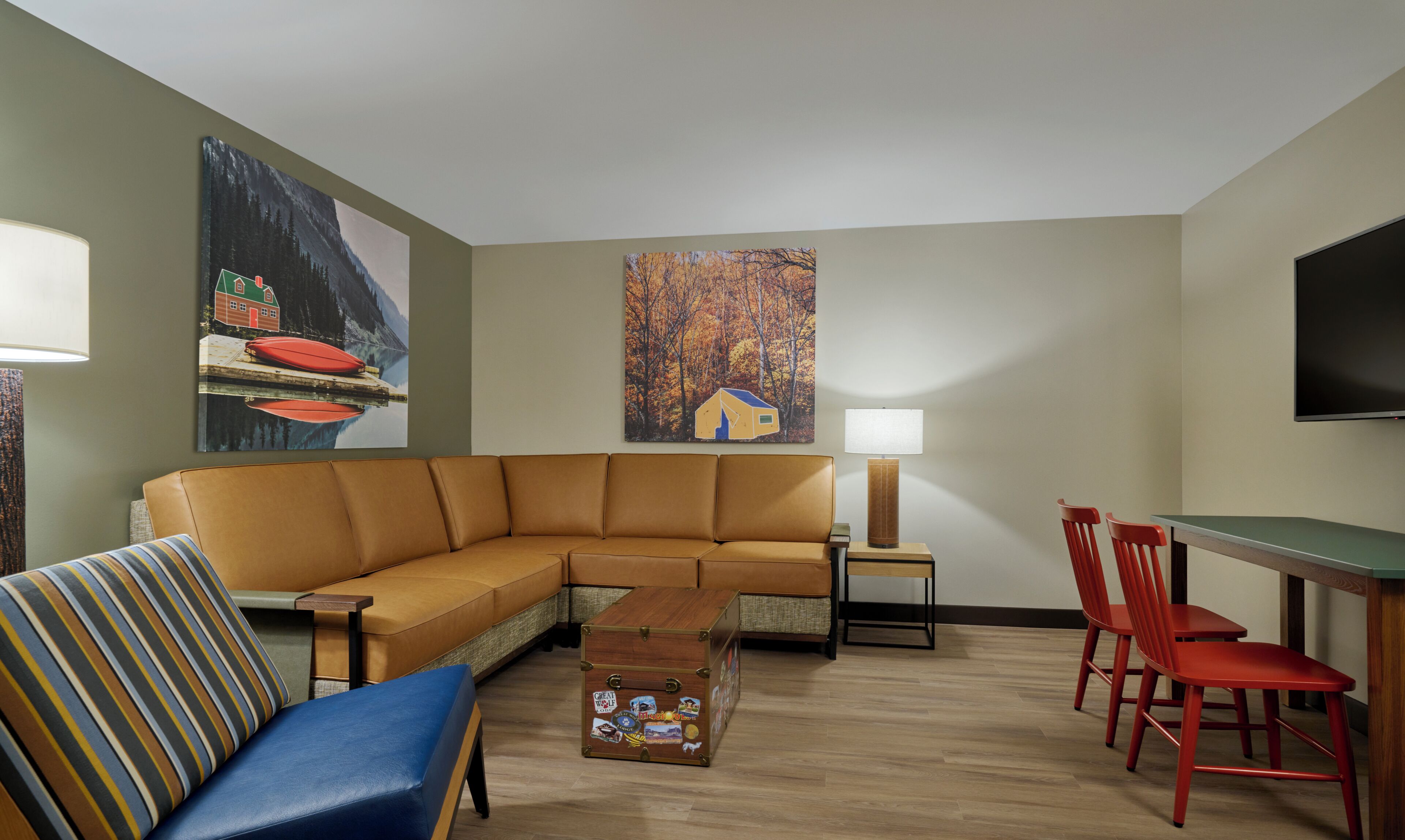 A living room with a sectional sofa, a small table, a lamp, a TV, and two red chairs.
