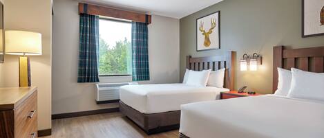 Une chambre d’hôtel avec deux lits, une commode en bois, une fenêtre avec des rideaux, une lampe fixée au mur et un tableau représentant un cerf.