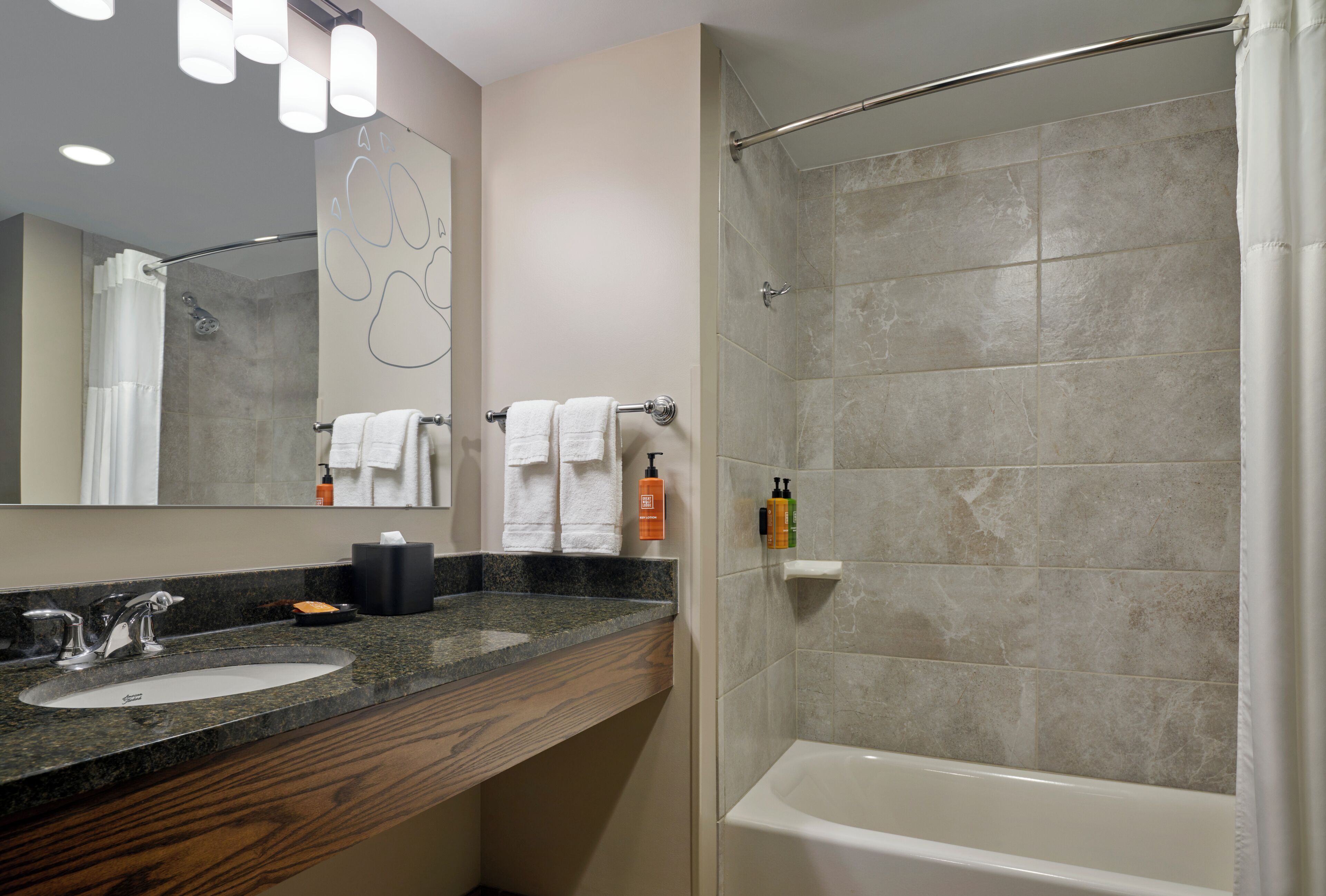 A bathroom with a sink, mirror, towel rack, shower, and toiletries.