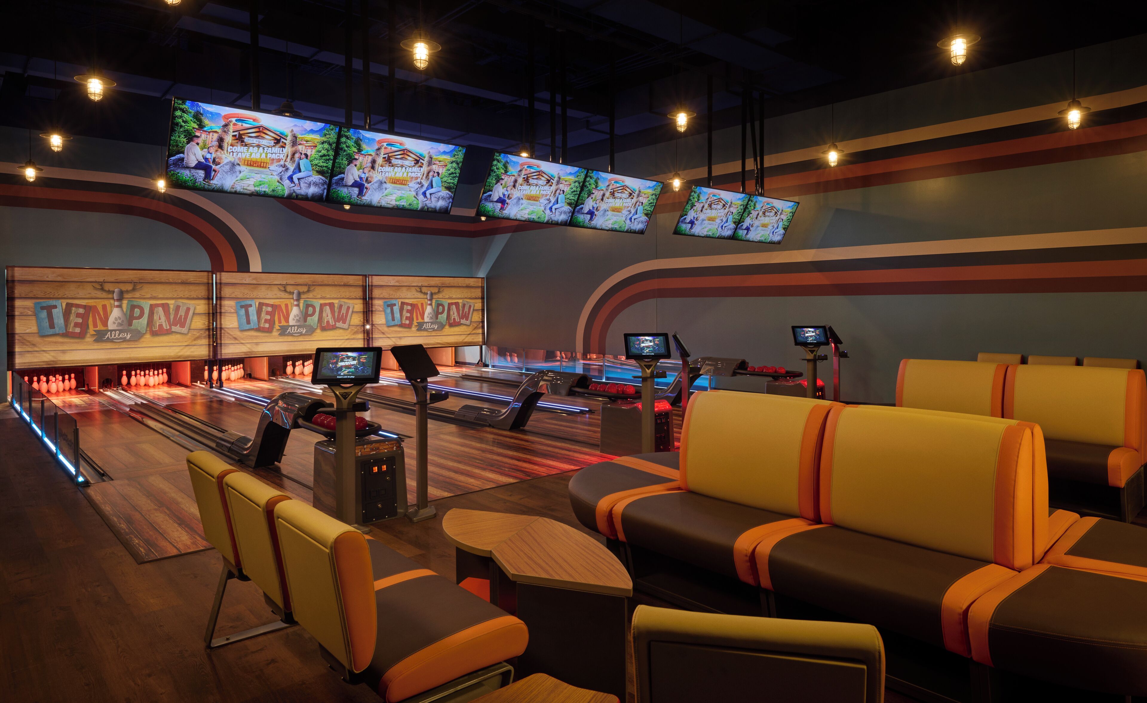 A bowling alley with multiple lanes, seating areas, and overhead screens displaying advertisements.