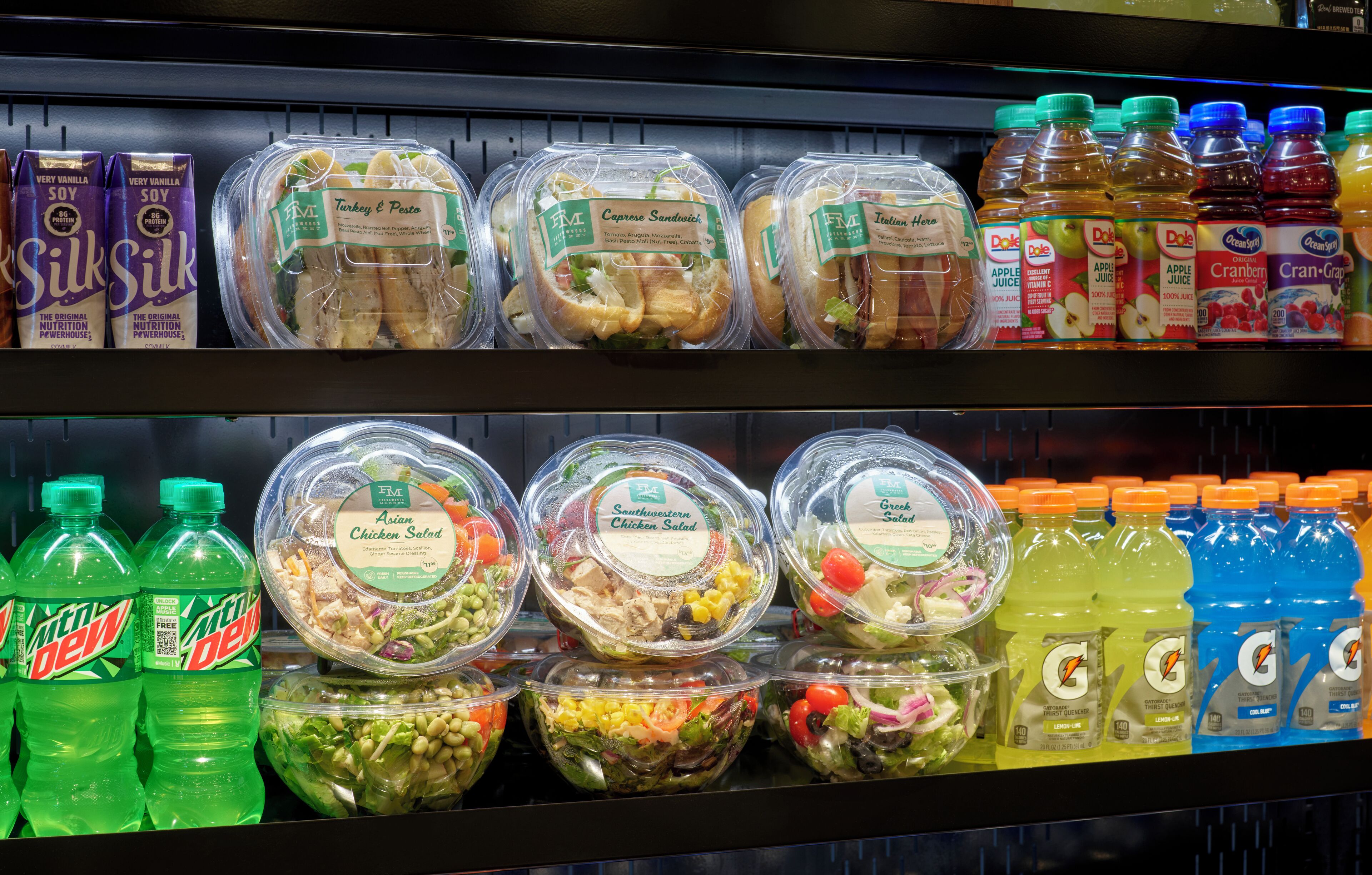 A refrigerated section with various food items including packaged salads, sandwiches, and beverages.