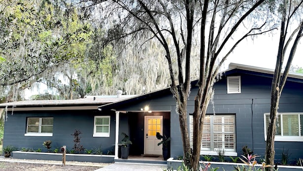 A modern two-story house with a dark exterior, a covered porch, and a well-maintained garden with various plants and a small tree.
