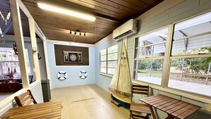 A room with wooden tables and chairs, a dartboard, life rings on the wall, and a sailboat model.