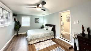 A bedroom with a bed, a ceiling fan, a nightstand, a dresser, and a door leading to another room.