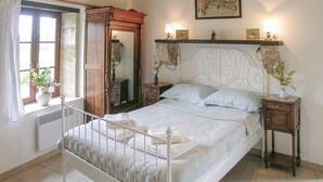 Ein Schlafzimmer mit Bett, Kommode, Spiegel und einem Fenster mit Vorhängen.