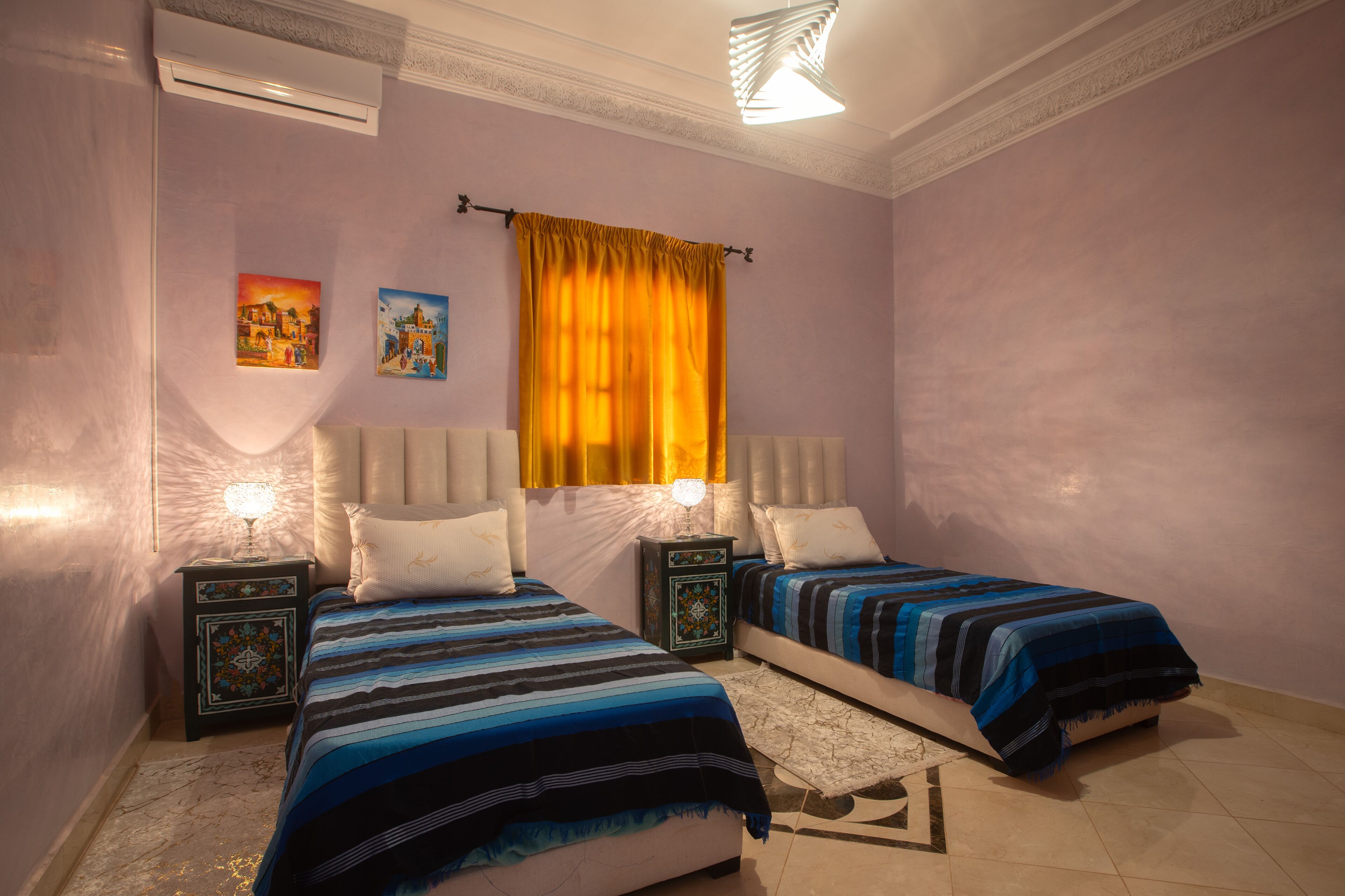 Un dormitorio con dos camas, una mesita de noche con lámpara, una ventana con cortinas amarillas y una obra de arte en la pared.