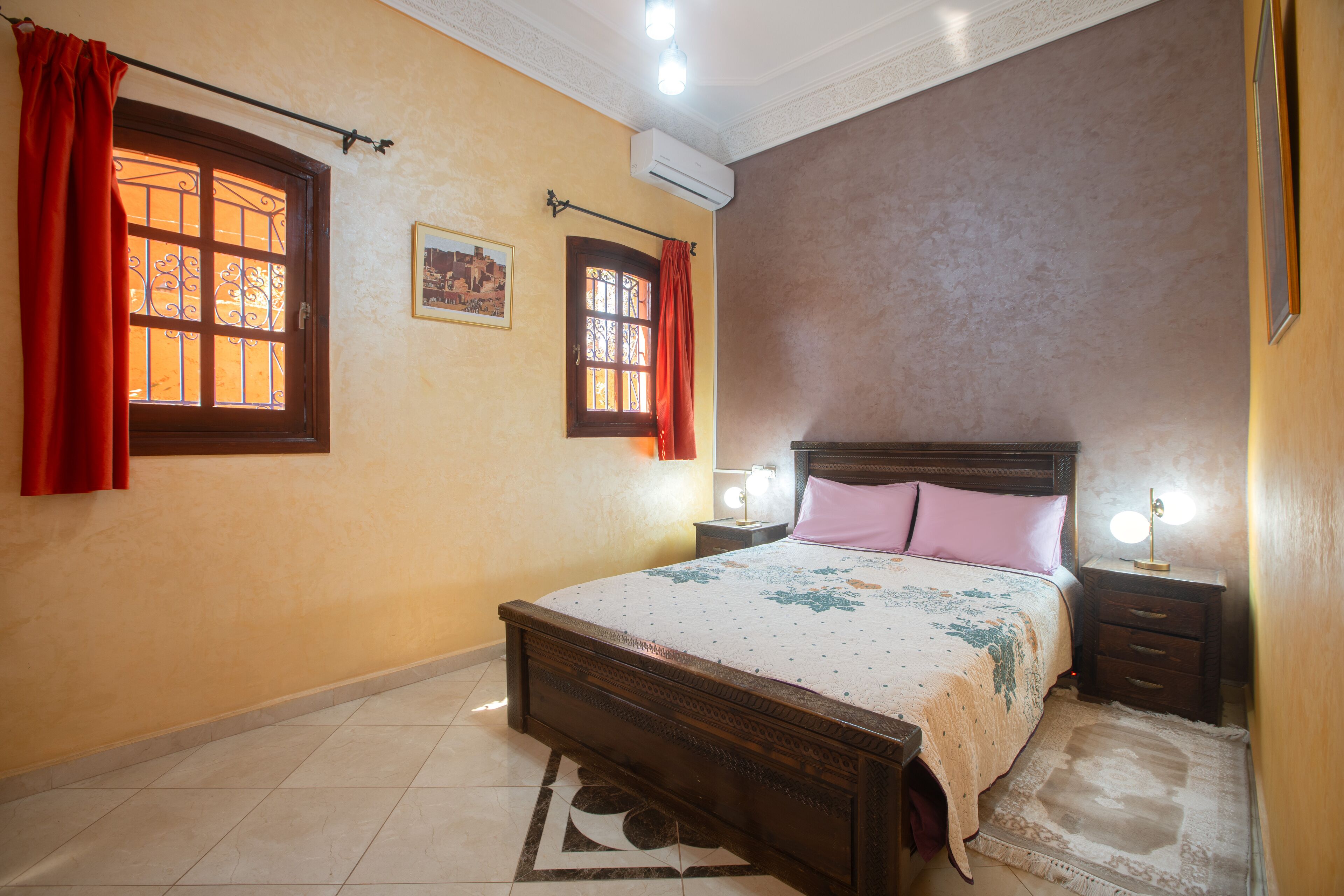 Une chambre à coucher avec un lit en bois, deux tables de chevet avec des lampes, un tapis et une fenêtre avec des rideaux.