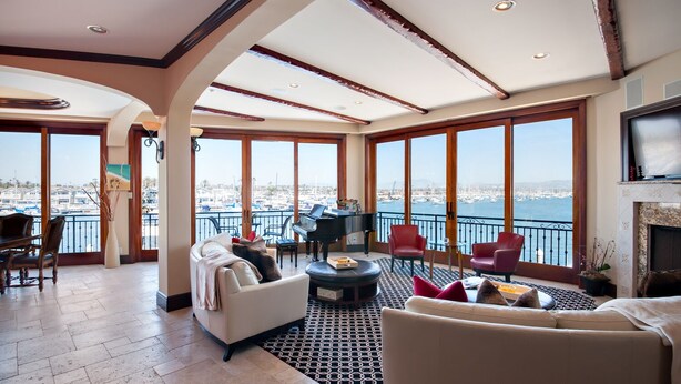 A spacious living room with a piano, a fireplace, and large windows offering a marina view. - 7 Bed Waterfront W/Rooftop pool & hot tub stunning 360-degree bay & beach view (Newport Beach)