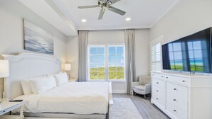 Een hotelkamer met een groot bed, een plafondventilator, een televisie, een raam met gordijnen en uitzicht op de omgeving.