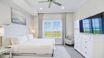 A hotel bedroom with a large bed, a ceiling fan, a TV, a window with curtains, and a view of the outdoors.