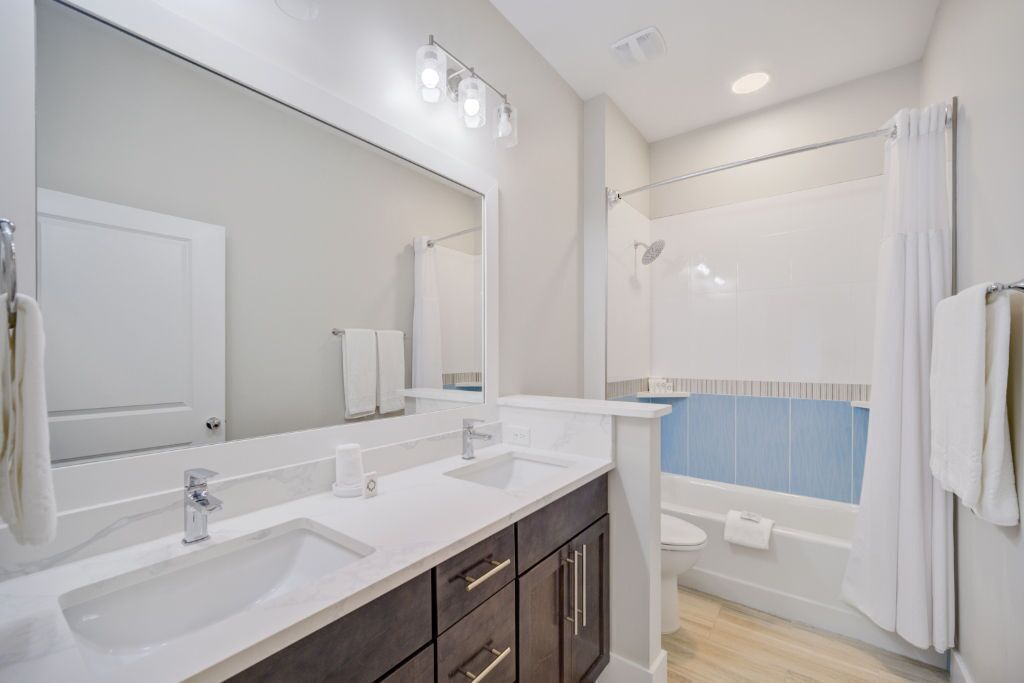 Un baño moderno con un espejo grande, dos lavamanos, una bañera y una ducha.