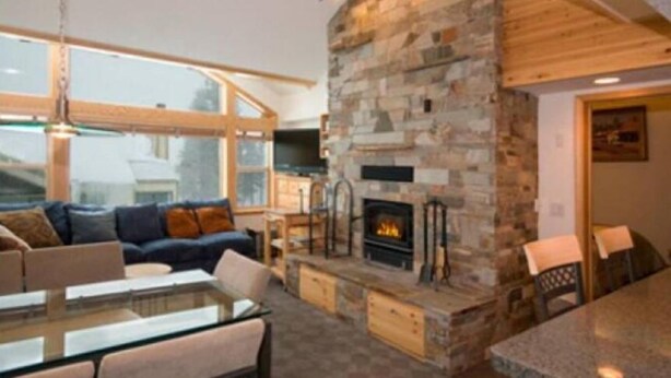 A modern living room with a stone fireplace, comfortable seating, and large windows. - 4 Bed + Loft, Gorgeous Kirkwood Condo (Kirkwood)