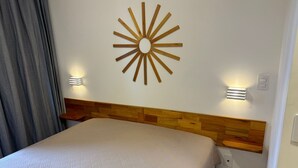 Ett hotellrum med en säng, ett träfärgat sänggavel, två vägglampor och ett dekorativt väggkonstverk i form av en solstråle.