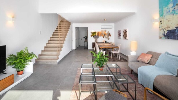 Um apartamento moderno com escada, área de jantar, sala de estar com sofá e mesa de centro, e uma TV à esquerda.