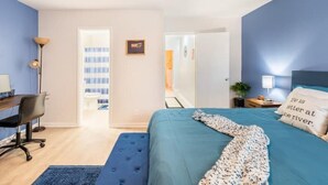 Un dormitorio con cama, escritorio y silla. Hay una puerta que da a otra habitación.