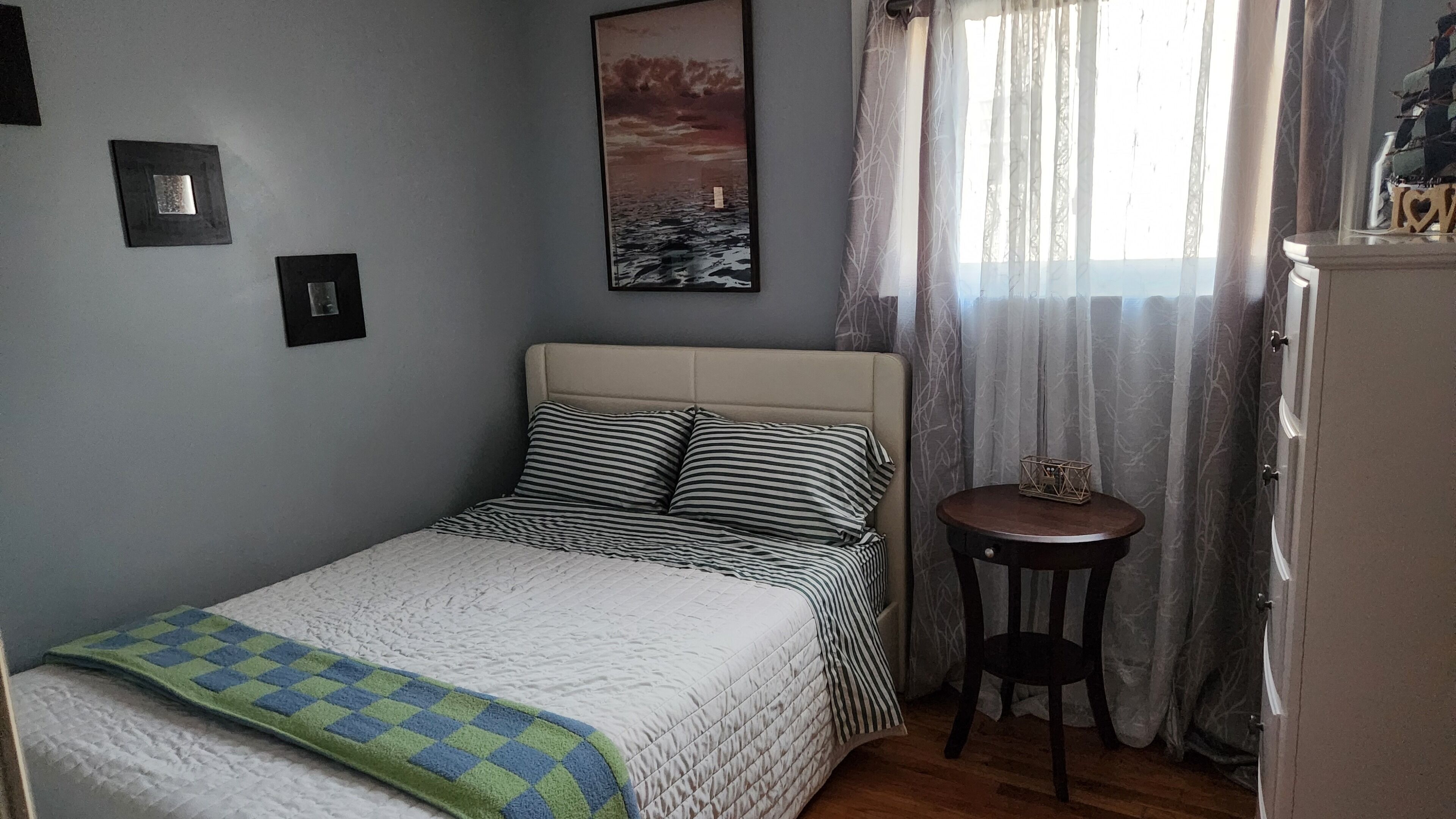 A bedroom with a bed, a small table, a cabinet, and a painting on the wall.