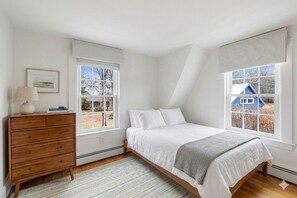 Un dormitorio con cama, cómoda y ventanas.
