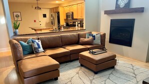 Un salon moderne avec un canapé d’angle en cuir marron, un pouf assorti et un tapis à motifs.