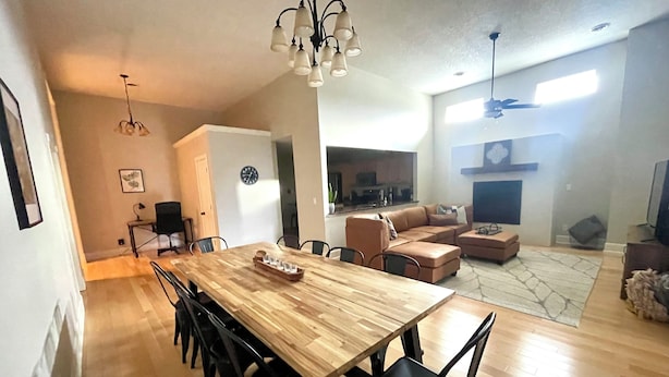 Un grand espace à manger avec une table en bois et des chaises noires, une cuisine en arrière-plan et un coin salon avec un canapé et un téléviseur.
