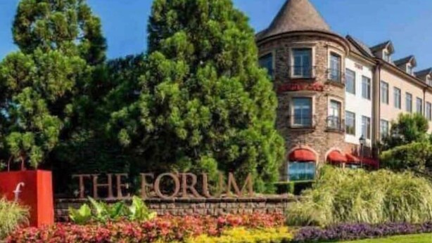Un bâtiment sur lequel on peut lire l’inscription « THE FORUM », entouré d’une végétation luxuriante et d’une variété de fleurs aux couleurs vives.