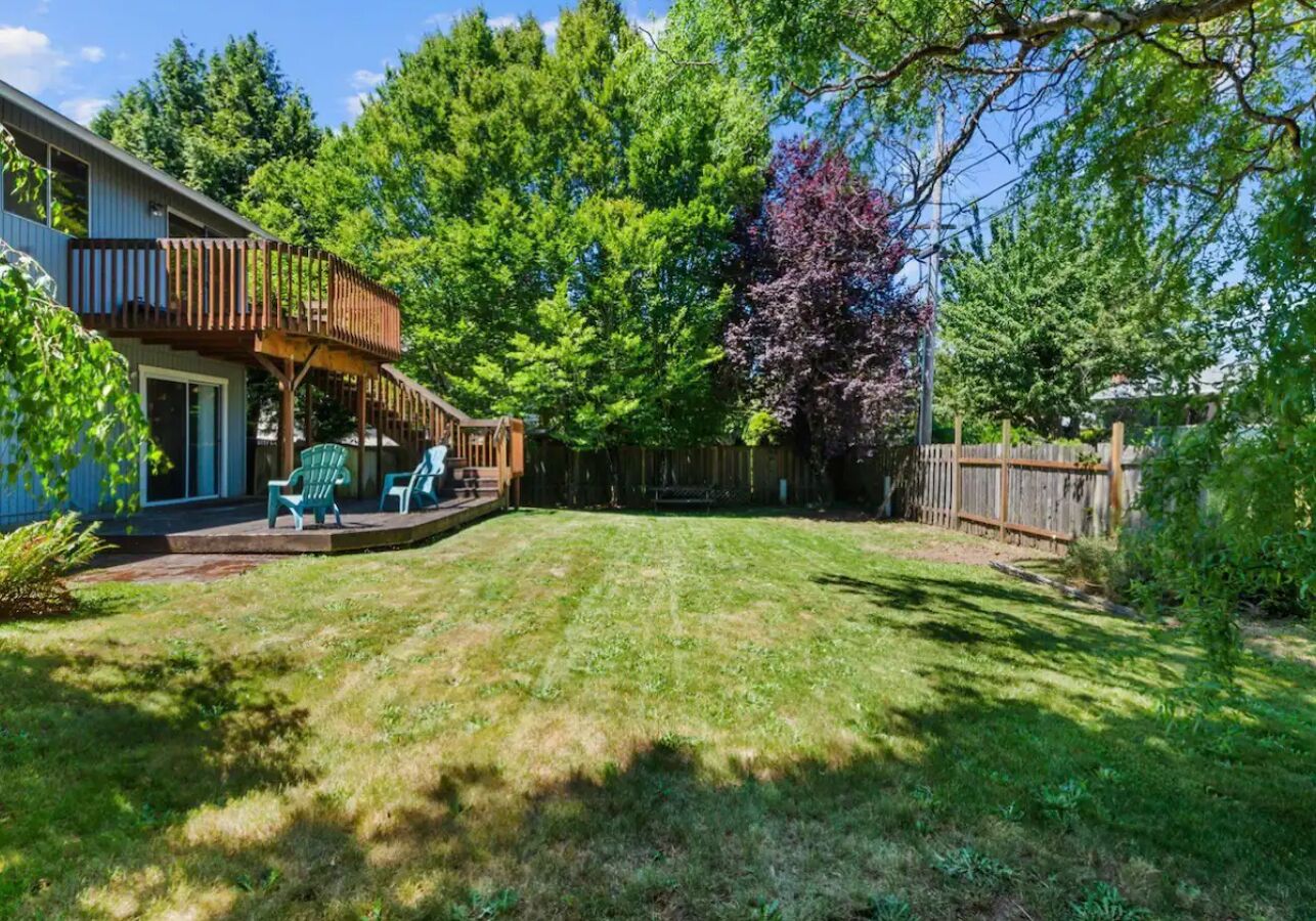 Un jardin avec une terrasse en bois, un patio couvert et une pelouse bien entretenue.