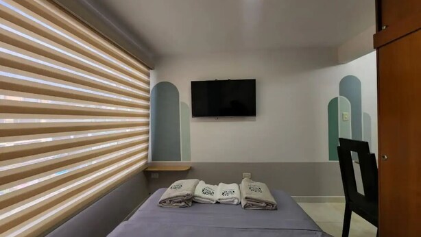 A hotel room with a bed, a TV mounted on the wall, and a window with blinds. - Apartment 10 Min Airport F

 (Bogotá)
