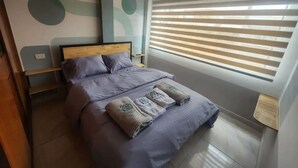 A bedroom with a wooden headboard, a bed with grey bedding, a nightstand, a wall with abstract art, and a window with blinds. - Apartment 10 Min Airport F

 (Bogotá)