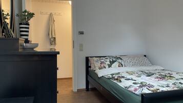 A bedroom with a bed, a dresser, a mirror, a potted plant, and a door leading to another room.