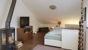 A cozy bedroom with a bed, a television, a fireplace, and a ceiling fan. - Wohnung in Idyllischem Örtchen (Meschede)