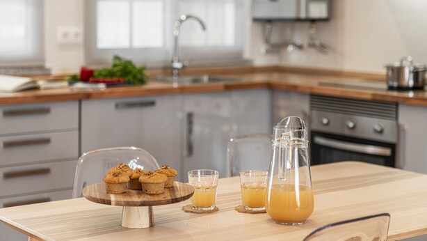 Una cocina con una mesa de madera, una jarra de vidrio y dos vasos de jugo de naranja.