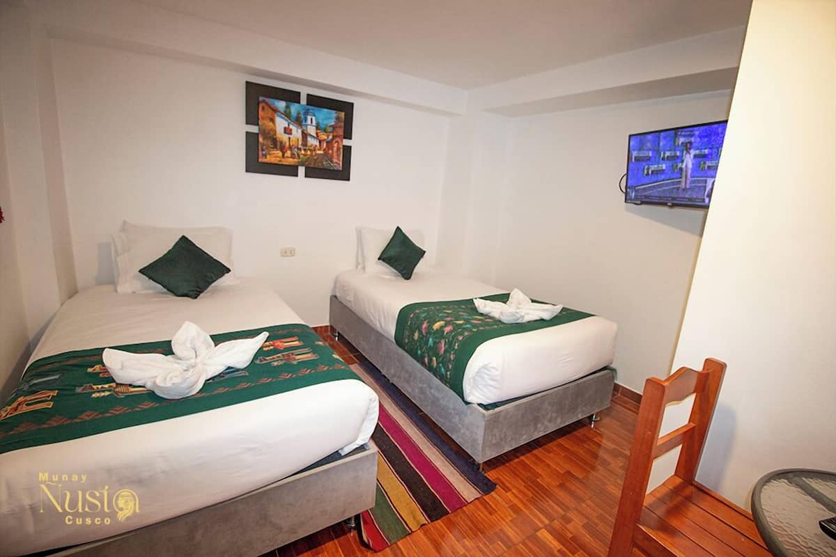 Quarto de hotel com duas camas, televisão e piso de madeira.
