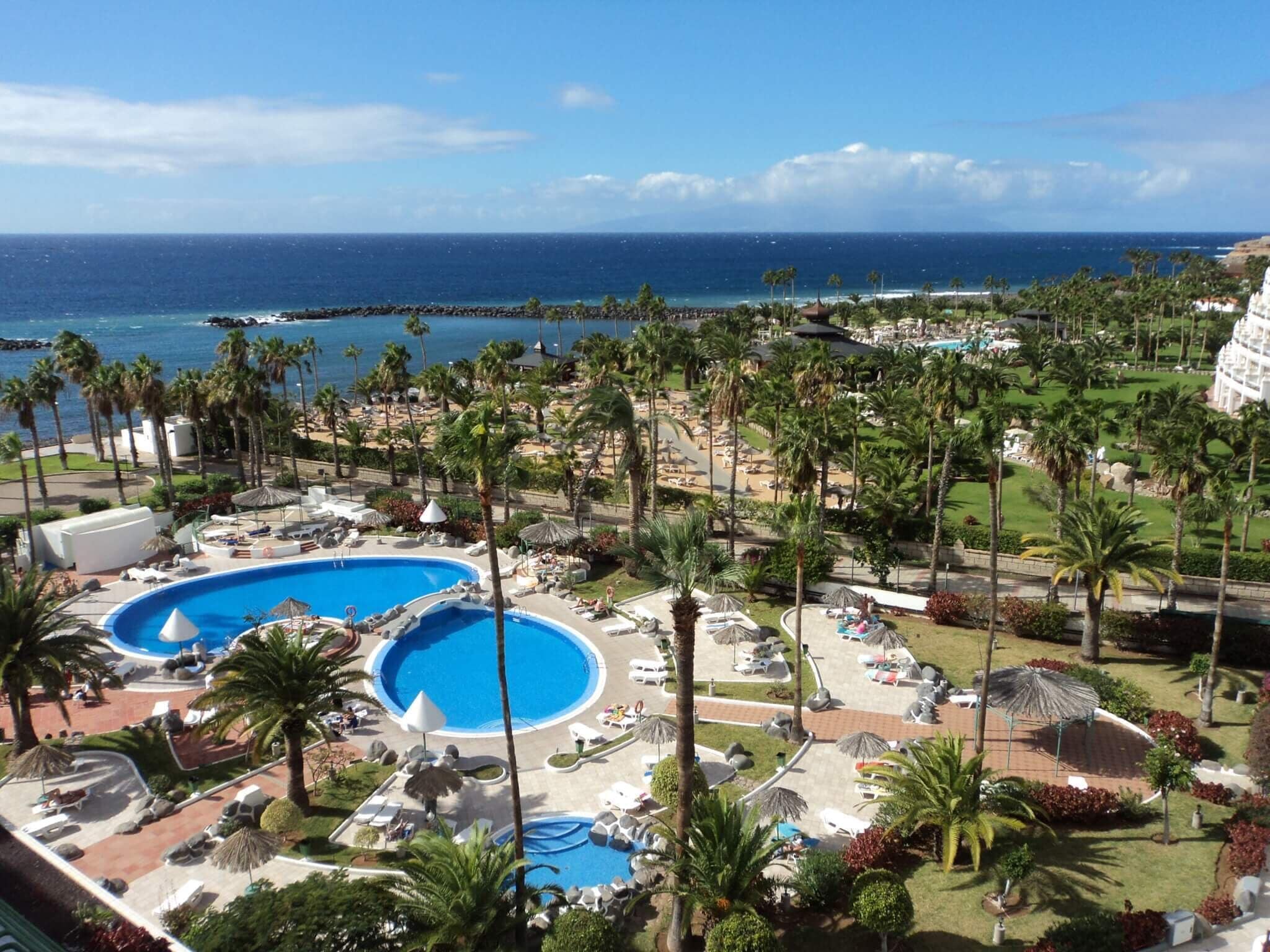 A resort with two large swimming pools, palm trees, and a view of the ocean.