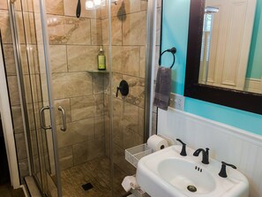 Bathroom features a glass-enclosed shower, handheld showerhead, and wall-mounted faucet.