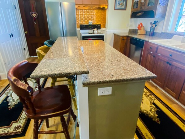 Une cuisine dotée d’un plan de travail en granit, de chaises en bois, d’un réfrigérateur et d’une cuisinière.