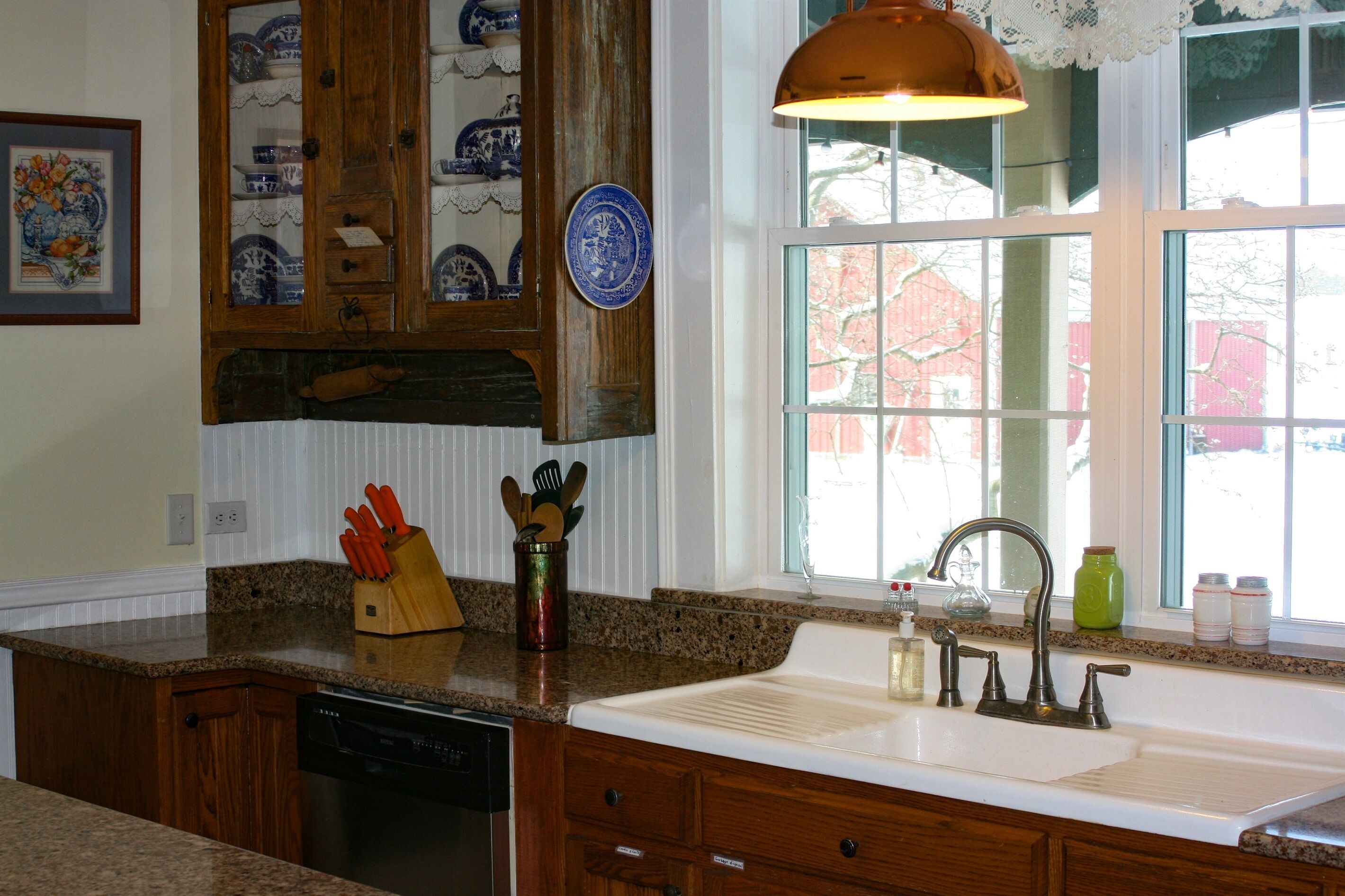 A kitchen with granite countertops, wooden cabinets, a built-in dishwasher, and a window with a view of a red building.