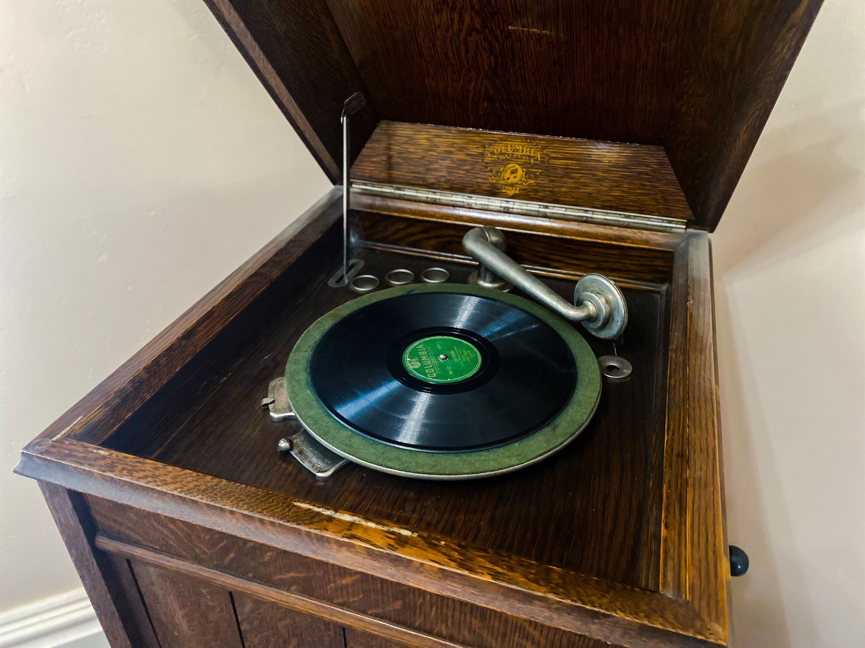 A vintage gramophone with a green record, placed inside a wooden cabinet with a hinged lid.