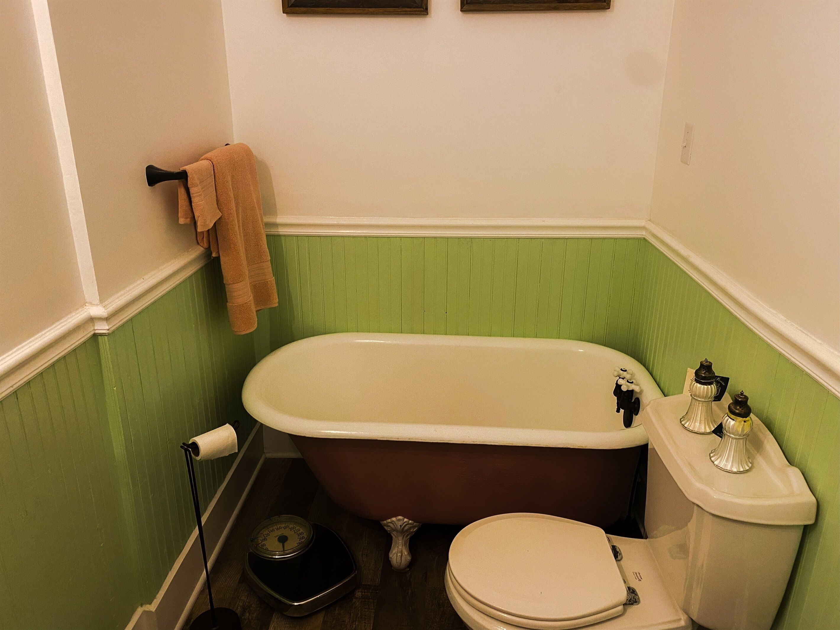 A bathroom with a freestanding bathtub, toilet, and a scale on the floor.