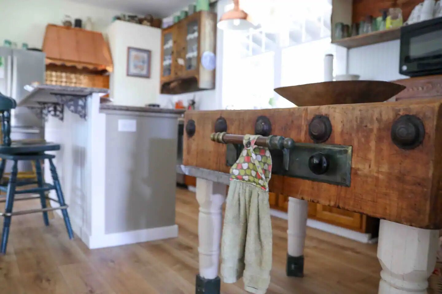 A kitchen with wooden cabinets, a refrigerator, a microwave, and a wooden table with a cloth.