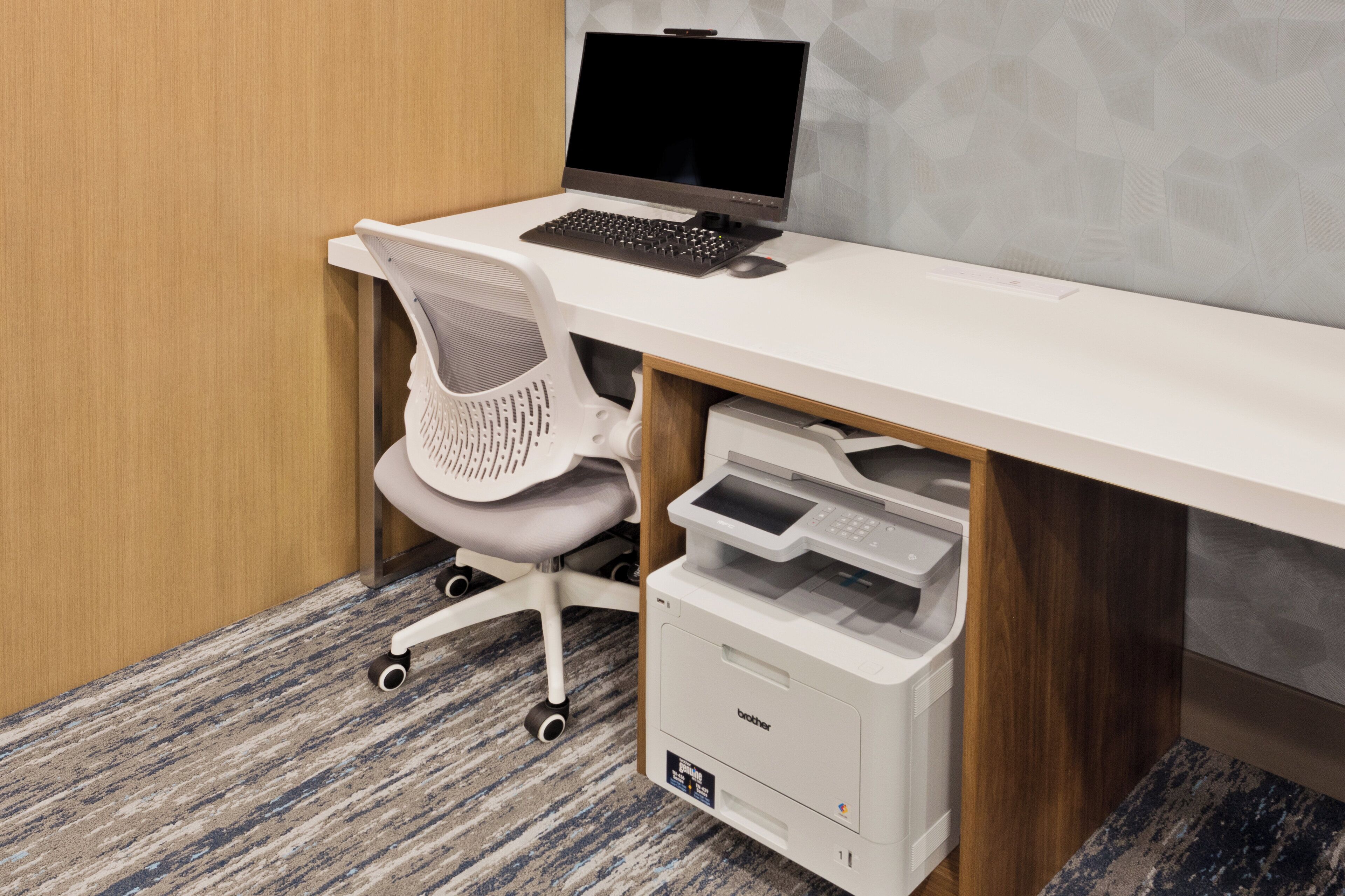 Ein moderner Schreibtisch mit einem Laptop, einem weißen Mesh-Stuhl und einem Brother-Drucker.