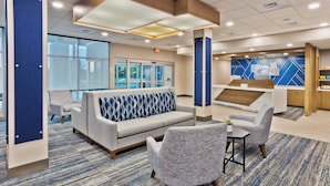 A modern hotel lobby with a seating area, a reception desk, and a view of the outside.