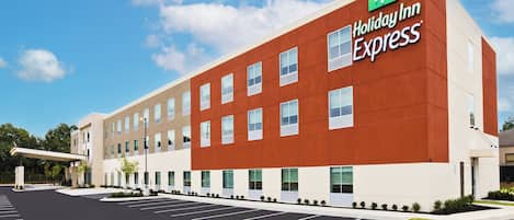 Un edificio de Holiday Inn Express con diseño moderno, que incluye una azotea plana y un amplio estacionamiento al frente.