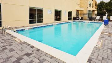 Una piscina rectangular con borde de baldosas, una escalera metálica y un patio de ladrillo.