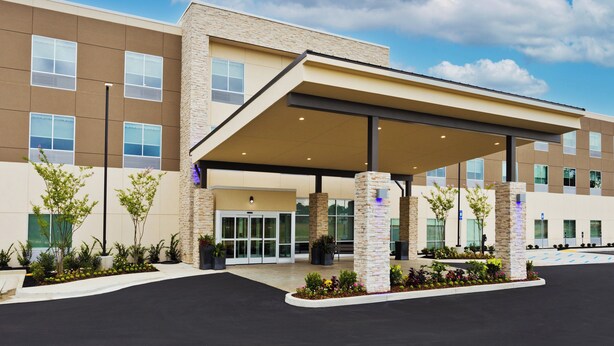 A modern hotel entrance with a covered waiting area, stone pillars, and a landscaped garden.