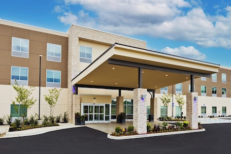 A modern hotel entrance with a covered waiting area, stone pillars, and a landscaped garden.