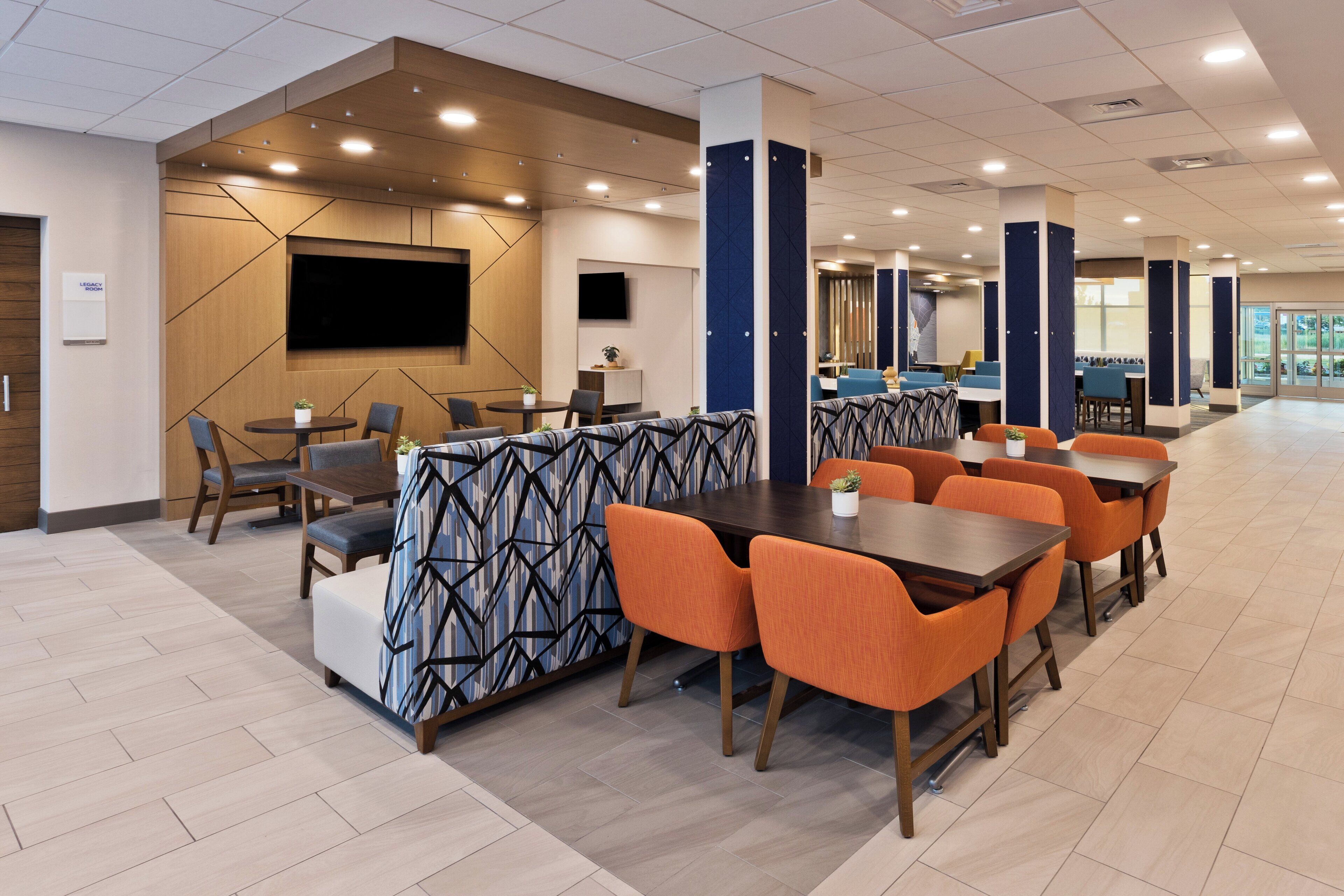 A modern dining area with a mix of seating options, including tables and booths, and a large flat-screen TV mounted on the wall.