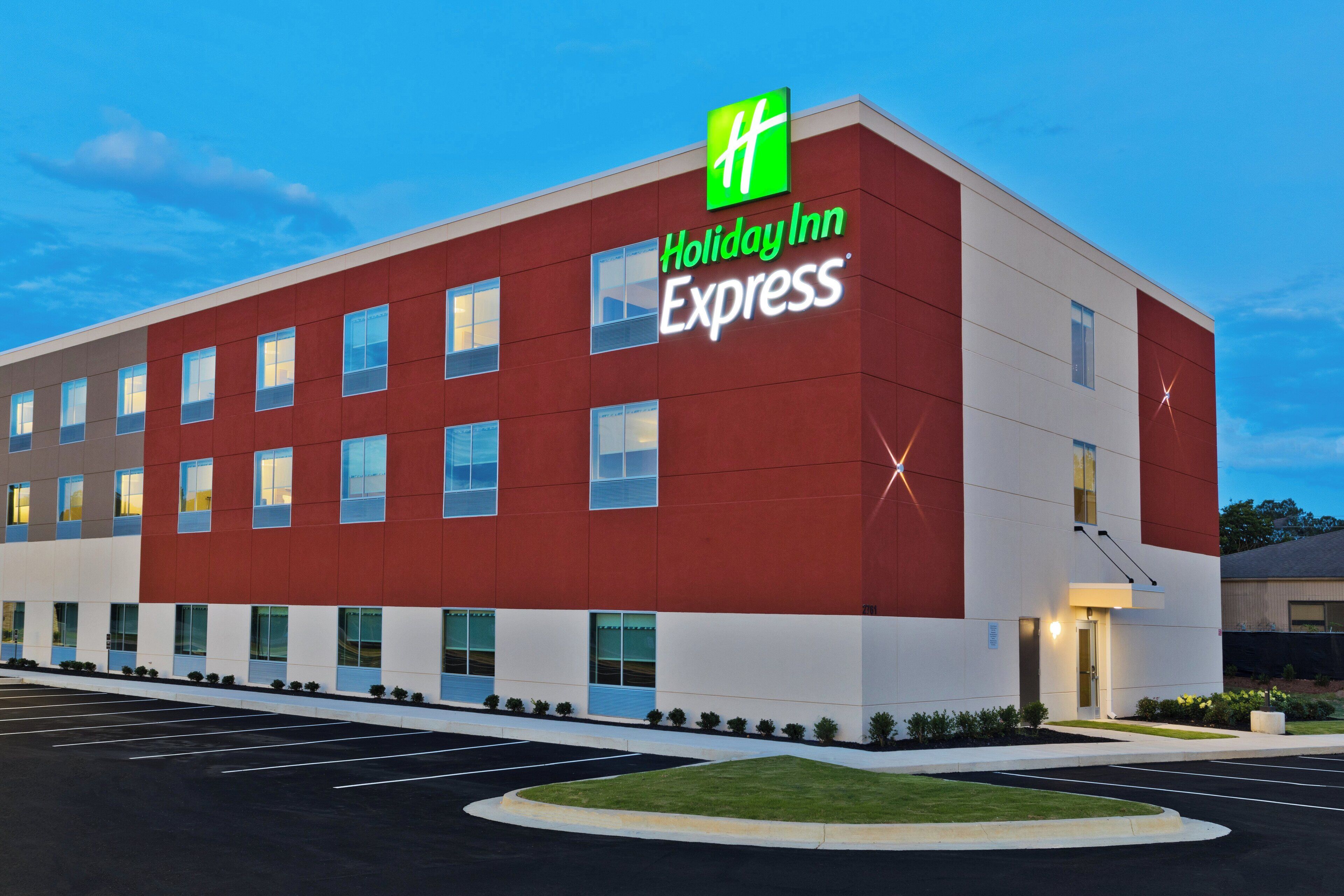 Edificio Holiday Inn Express con fachada roja, múltiples ventanas y un estacionamiento.