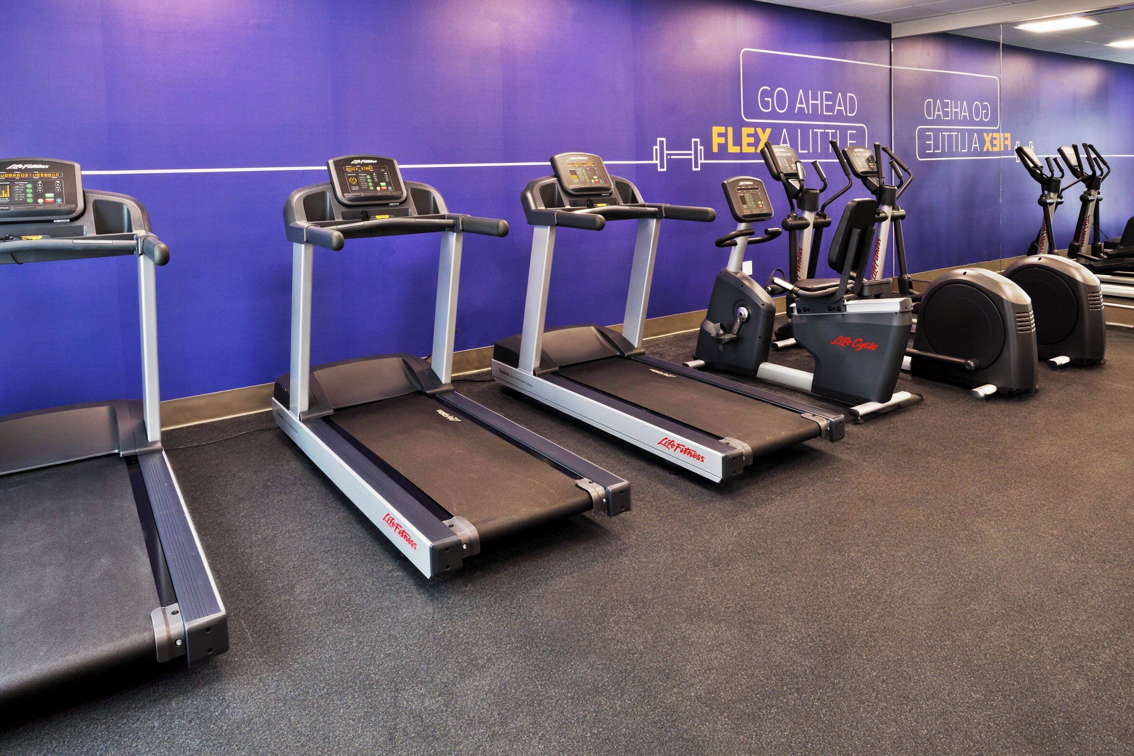 A gym with treadmills, ellipticals, and a mirrored wall with motivational text.