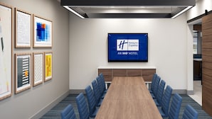 A conference room with a long table, blue chairs, framed artwork on the walls, and a large screen displaying the Holiday Inn Express logo.